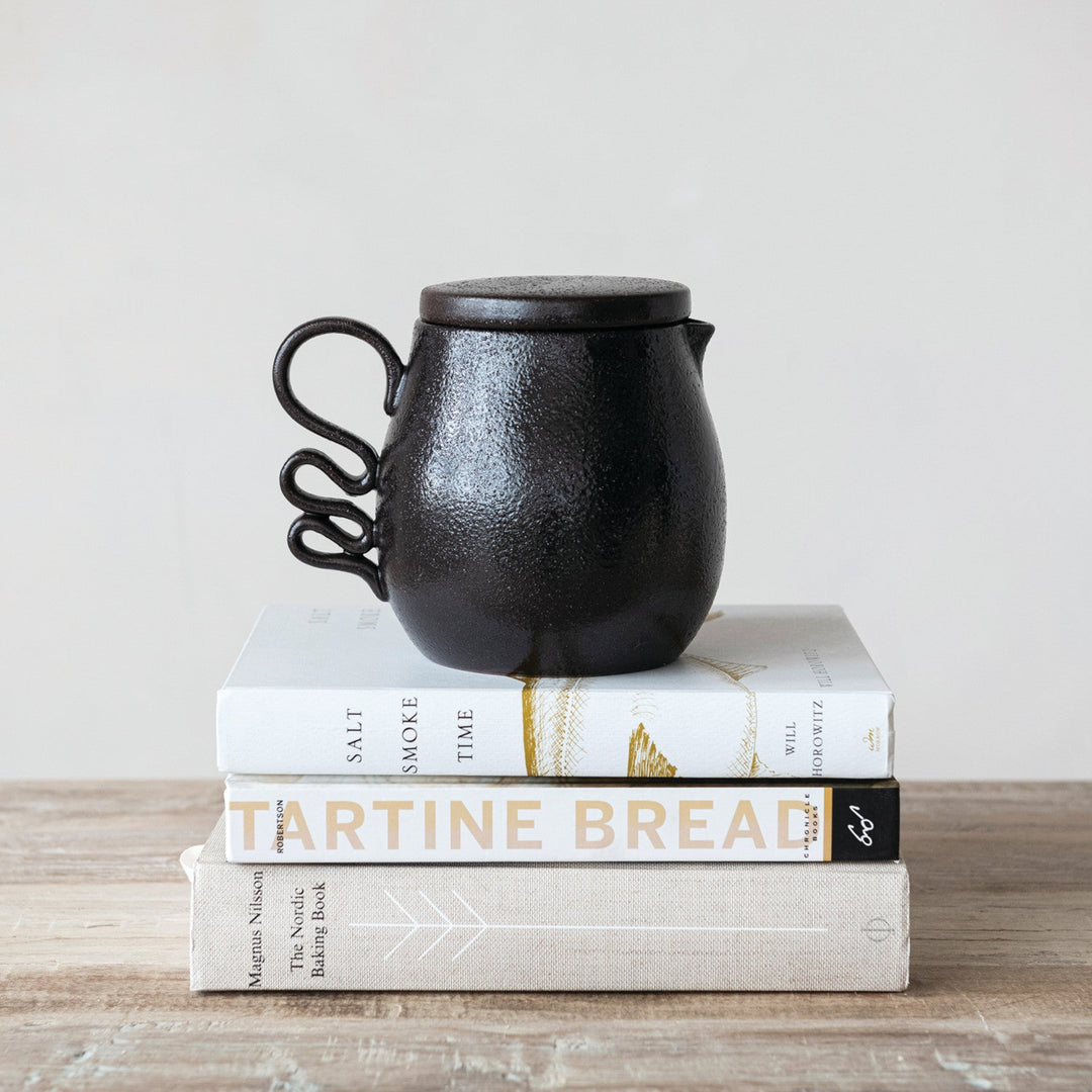 Black ceramic teapot on a stack of books with a light background