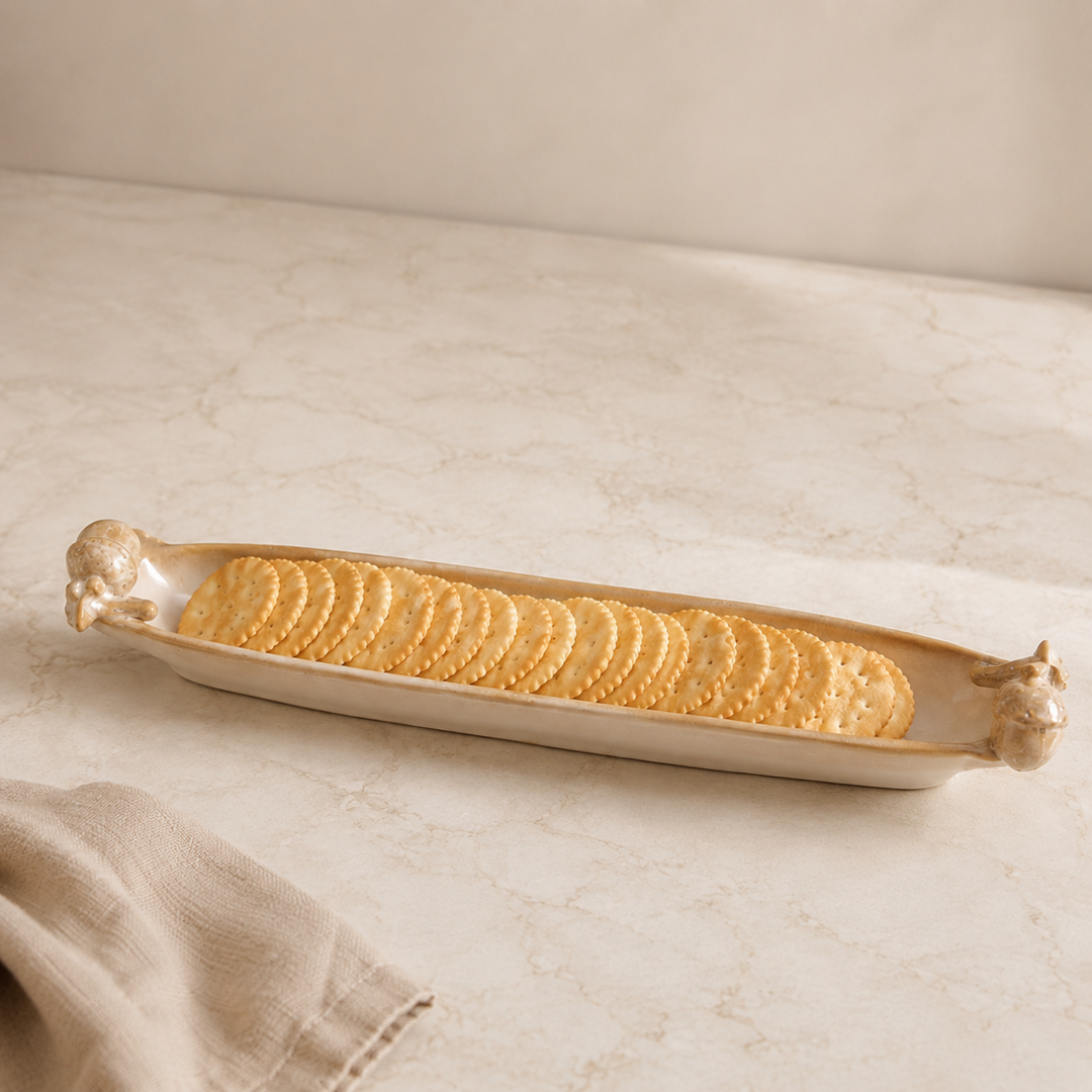 Rectangular ceramic tray with animal handles holding crackers on a beige surface.