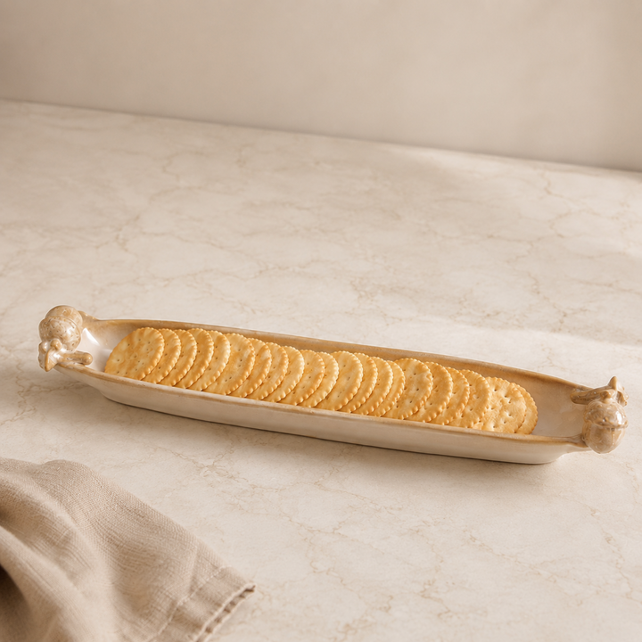 Rectangular ceramic tray with animal handles holding crackers on a beige surface.