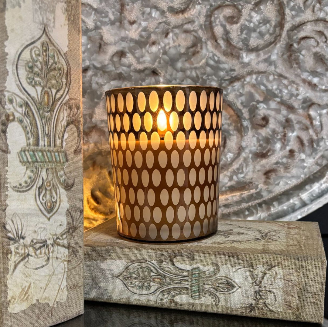 Decorative candle holder with a lit candle on top of ornate books against a textured wall.