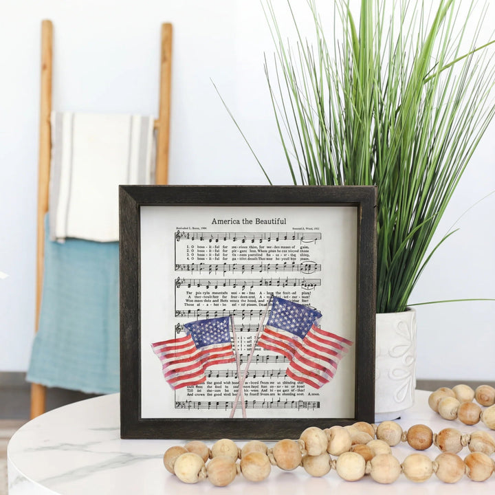 Framed sheet music with American flags on a table with decorative items.