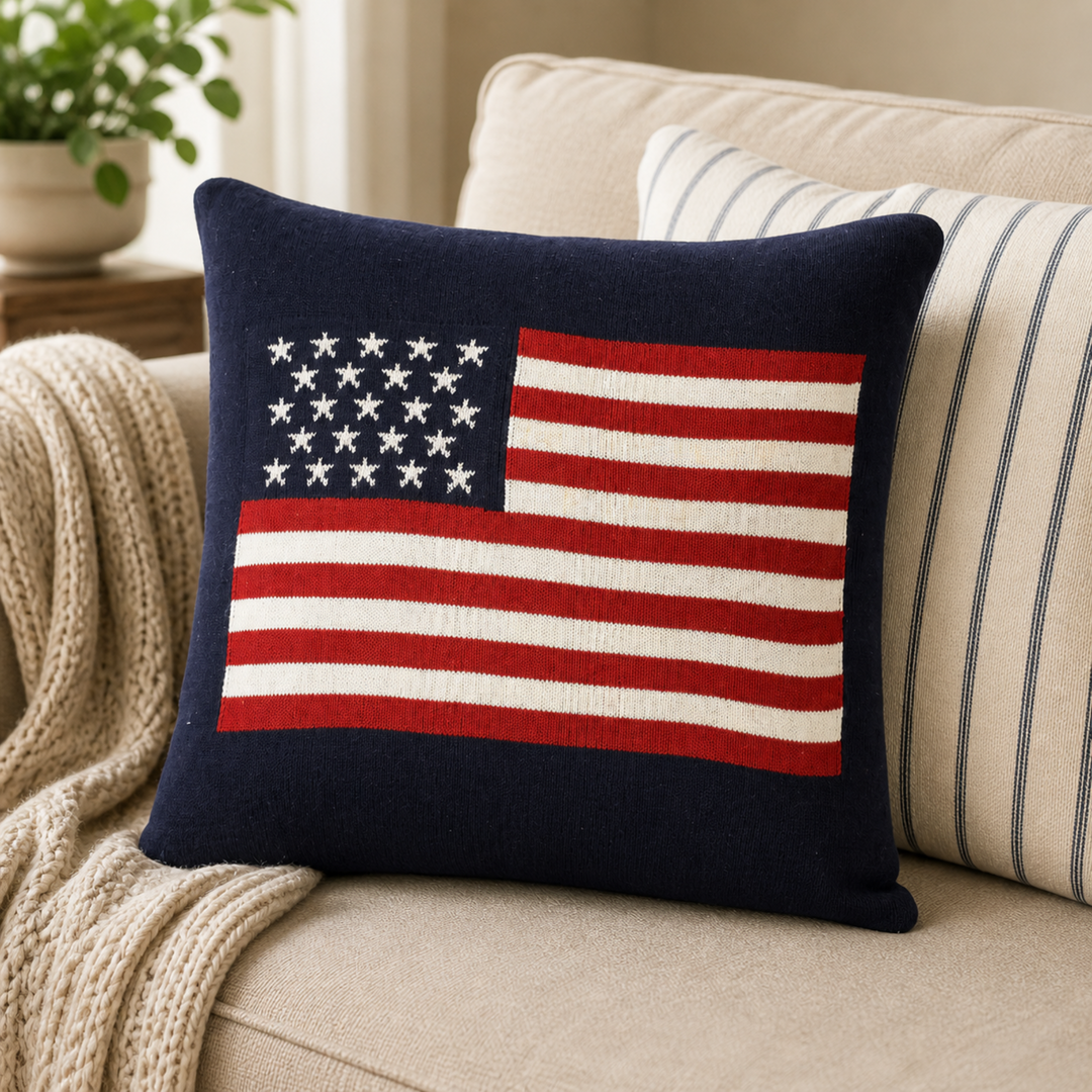 American flag pillow on a beige couch with a striped pillow and plant in the background