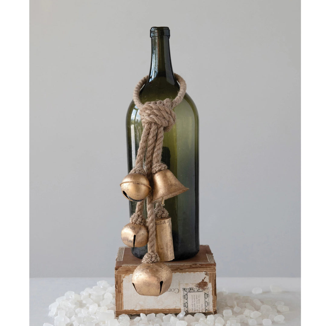 Decorative bottle with gold bells and rope on a white surface
