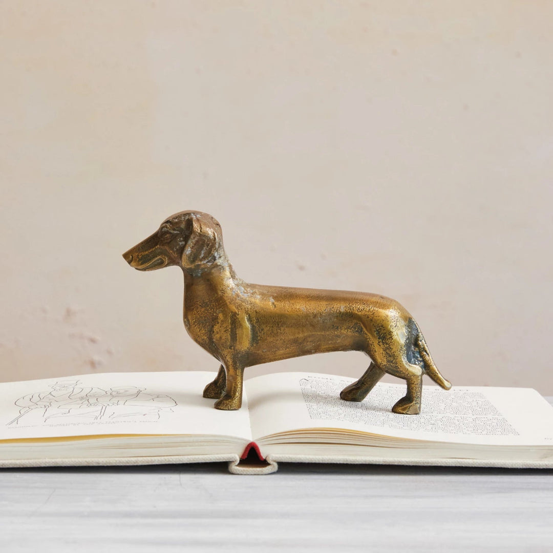 A brass-finished cast aluminum Dachshund figurine placed on an open book.