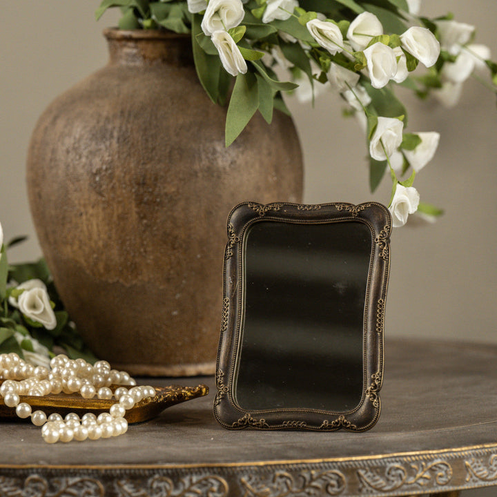 Decorative mirror with ornate frame on a table with a vase and flowers in the background