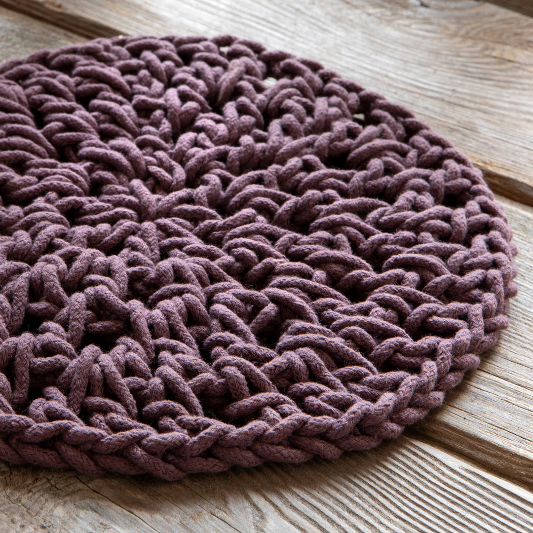 Round knitted mat in purple on a wooden surface