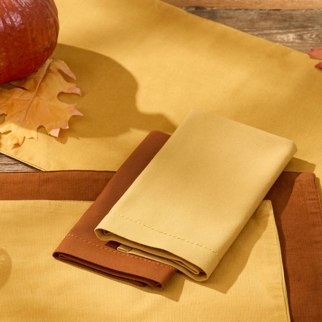 Two wallets, one brown and one beige, on a yellow fabric background with a pumpkin and leaf.