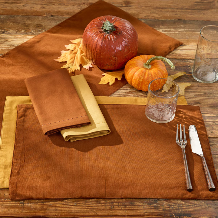 Autumn-themed table setting with pumpkins, leaves, and cutlery on a wooden table.