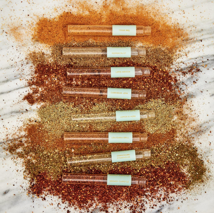 Set of small transparent bottles with green labels on a surface with gold and red powders.