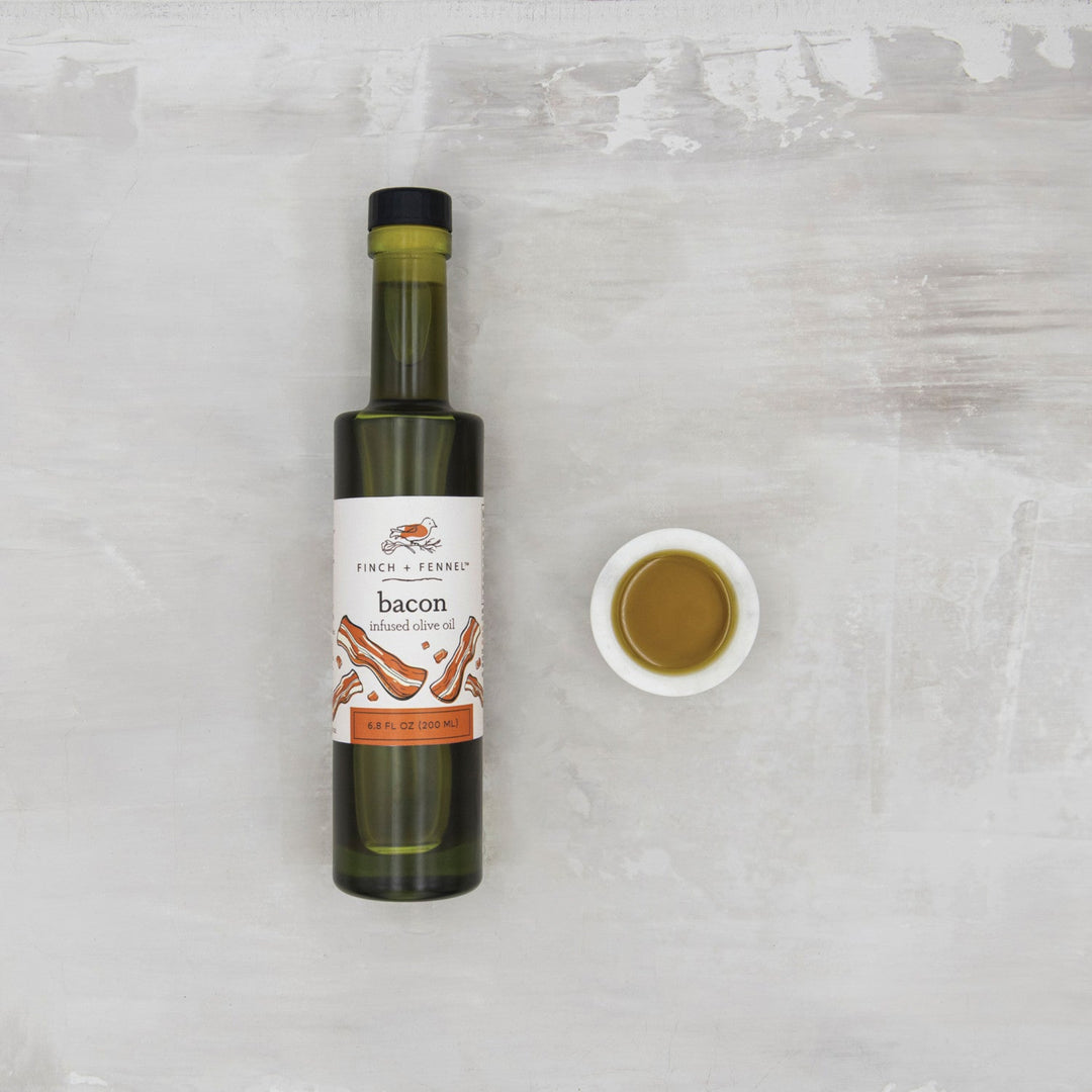 Bottle of 'bacon' flavored olive oil with a small dish of oil on a textured white surface