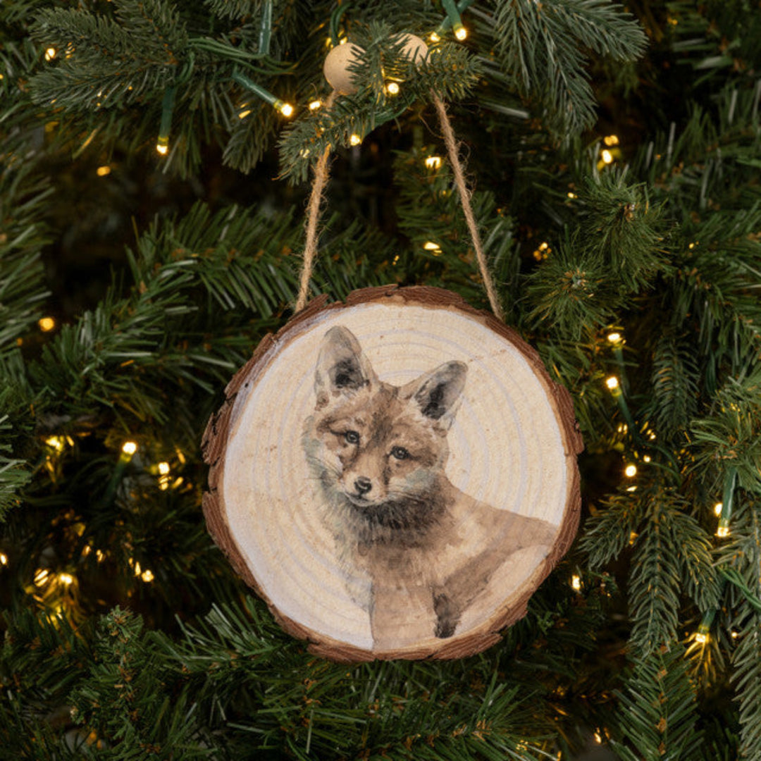 Wooden ornament with a fox design hanging on a Christmas tree.