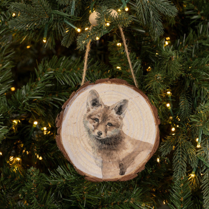 Wooden ornament with a fox design hanging on a Christmas tree.
