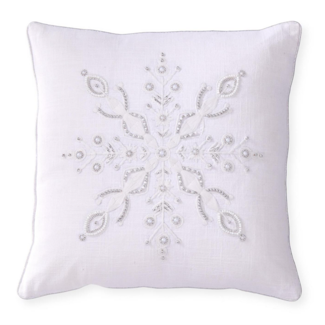 A square white throw pillow featuring an intricate white embroidered snowflake design with pearl-like bead accents, shown against a plain white background.