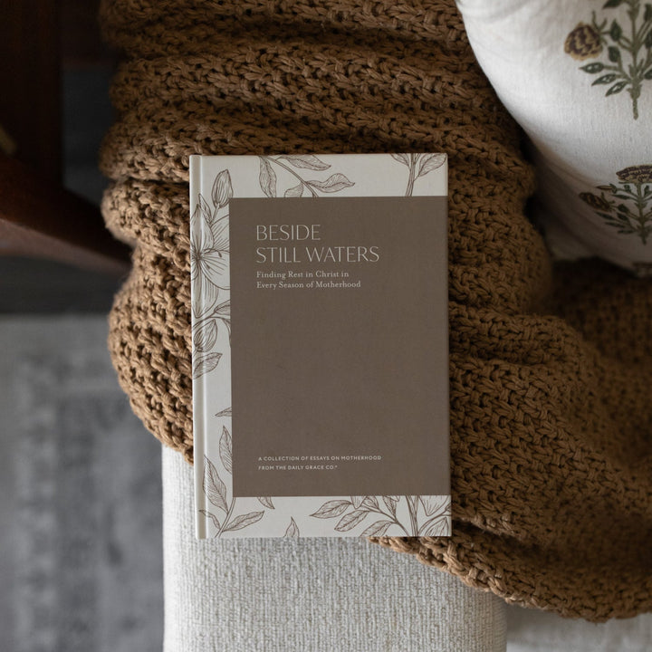 Book titled 'Beside Still Waters' on a textured surface with a knit blanket.