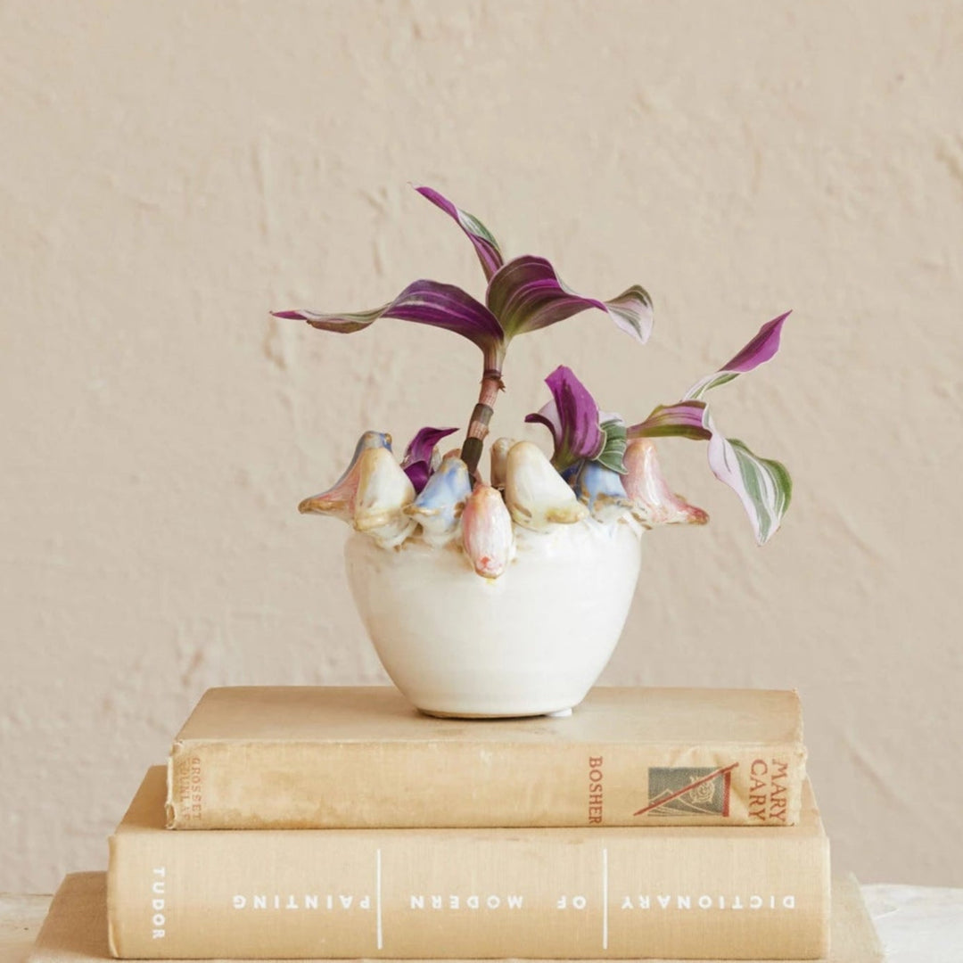 Small white vase with flowers on top of stacked books against a beige wall.