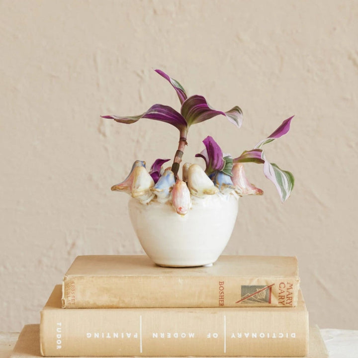 Small white vase with flowers on top of stacked books against a beige wall.