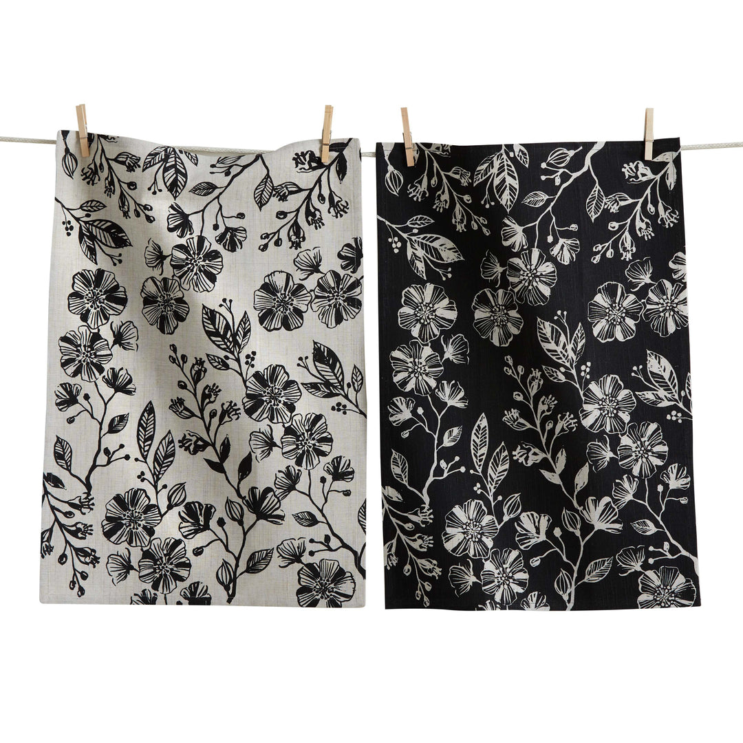 Two floral-patterned towels hanging on a clothesline, one white with black flowers and the other black with white flowers.