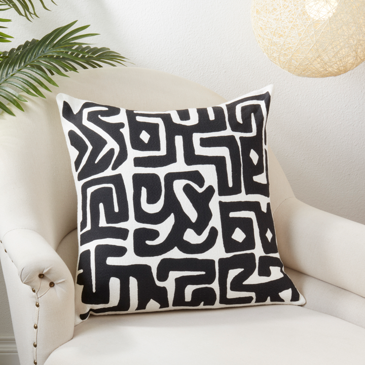 Decorative pillow with black geometric pattern on a white armchair.