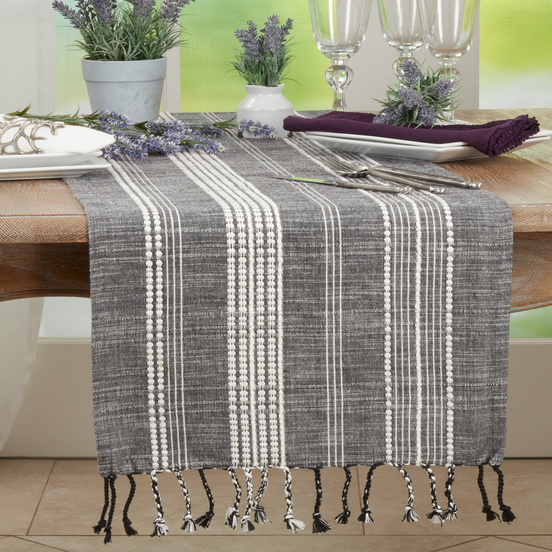 Gray and white striped table runner with tassels on a wooden table.