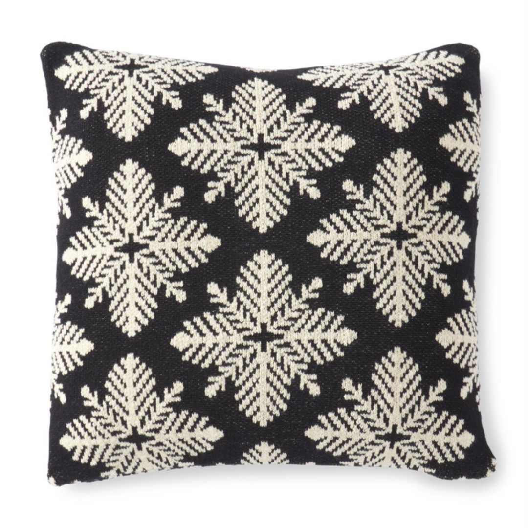 A square throw pillow featuring a black and cream woven snowflake pattern, photographed against a clean white background.