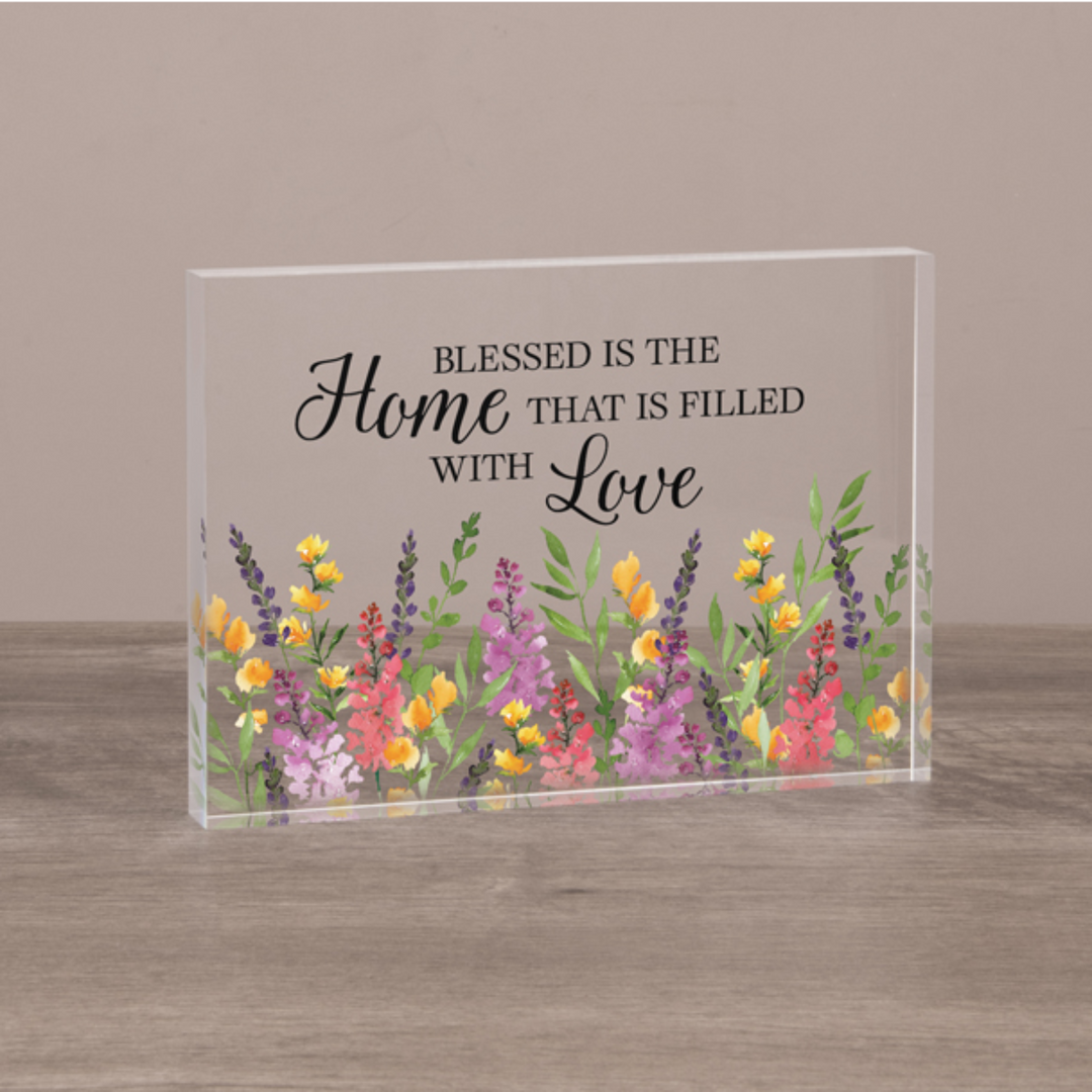 Decorative glass block with floral design and text on a wooden surface.