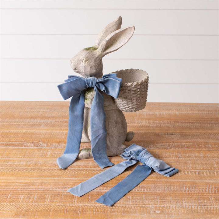 Decorative rabbit figure with a blue bow and basket on a wooden surface