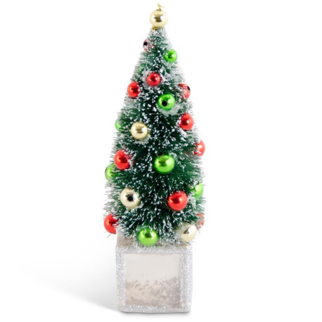A small artificial Christmas tree with a frosted green and white textured finish, decorated with shiny red, green, and gold ornaments, standing on a glittery silver base against a white background.