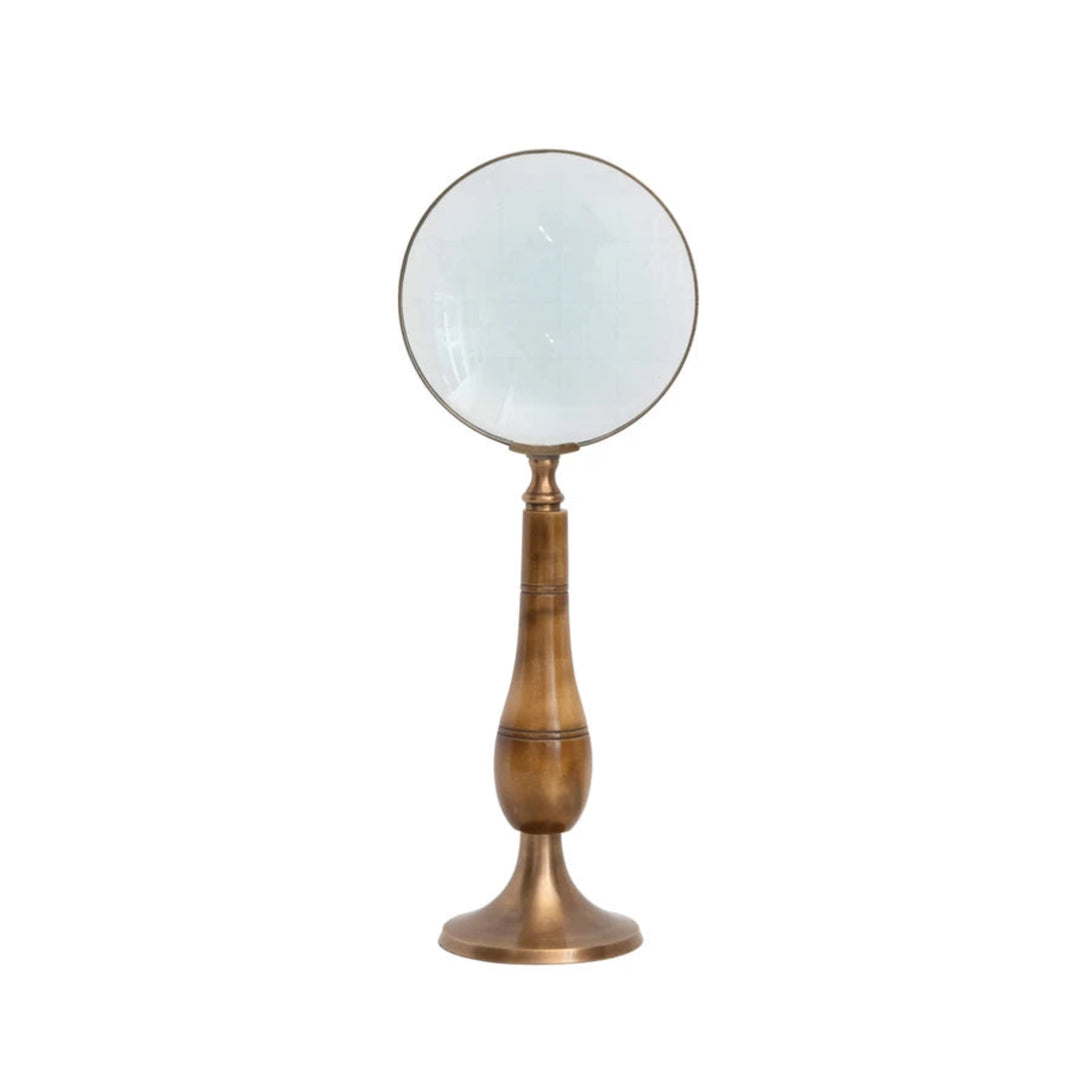 A brass and bone magnifying glass with a round flat base standing on a cylindrical stem with a flared antique finish.