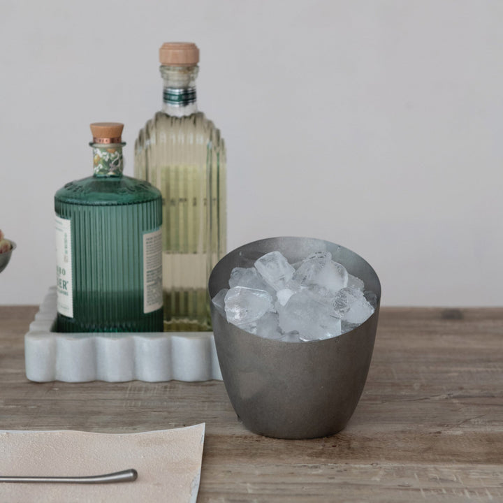 Bottle of gin with a bottle of vodka and a bowl of ice on a wooden surface.