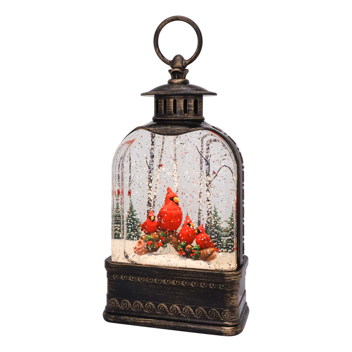 A decorative lantern-shaped snow globe with a dark bronze metal frame, featuring a winter forest scene with red cardinals, evergreen trees, and falling snow inside a clear glass dome, set against a plain white background.