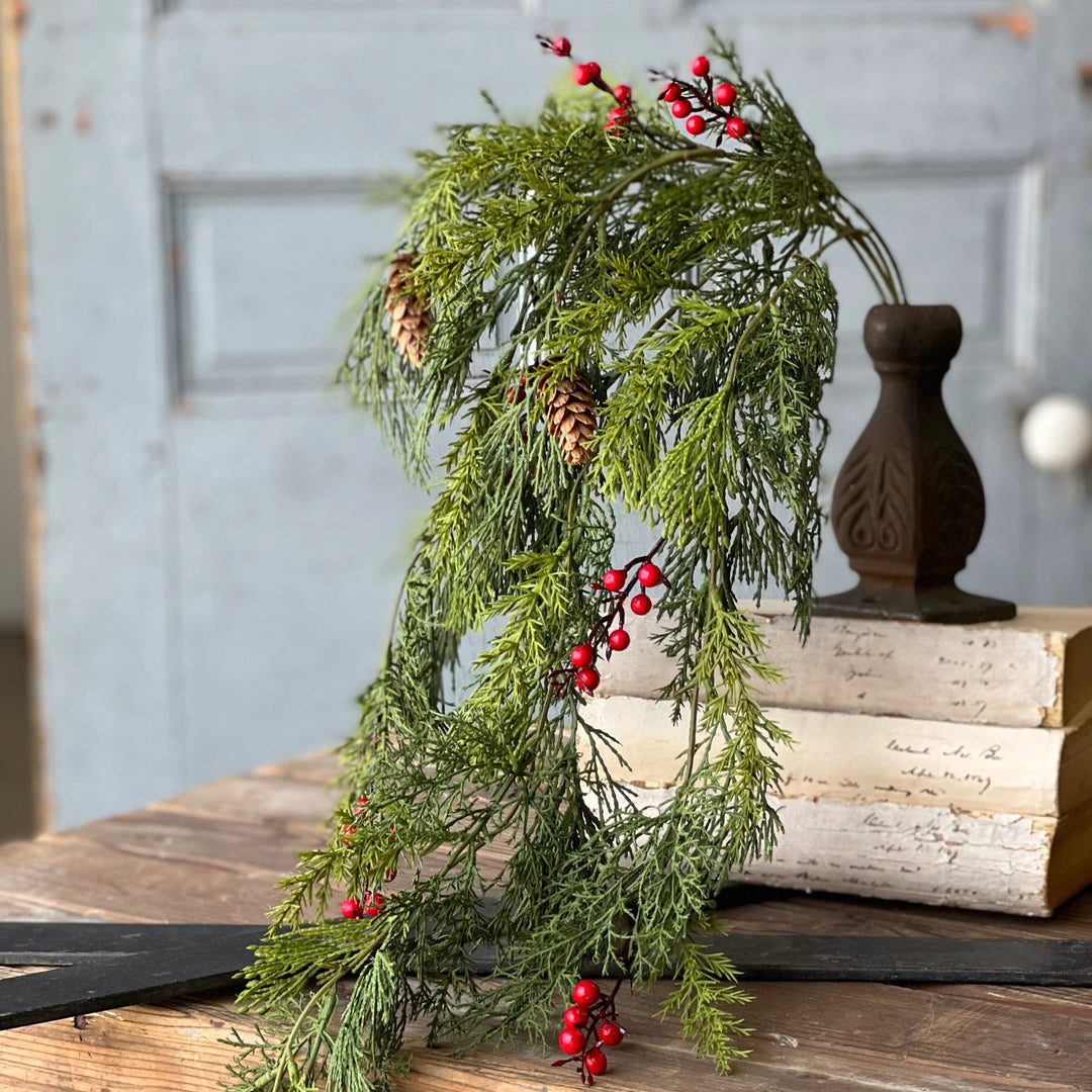 Decorative arrangement of greenery with red berries on a wooden surface with books and a vase.
