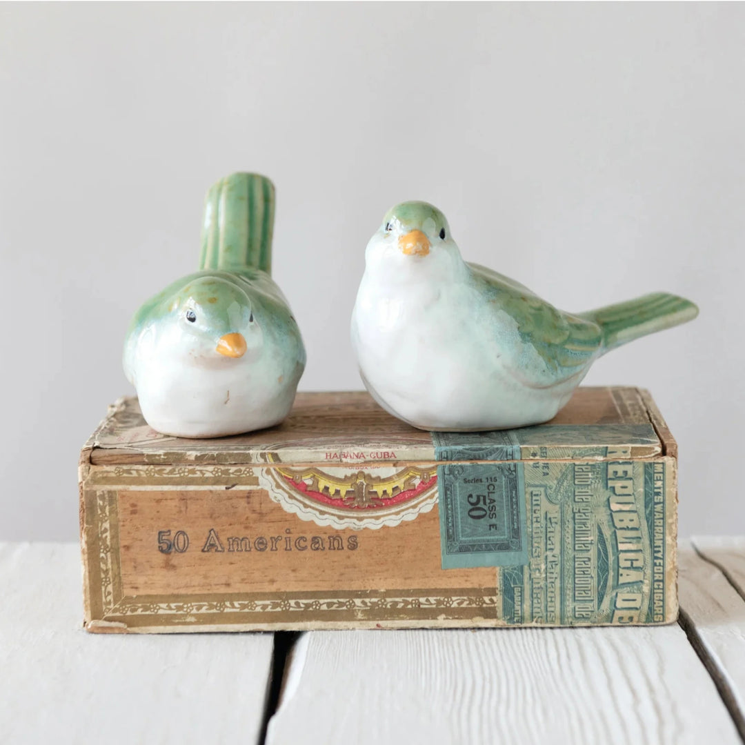 Two ceramic bird figurines on top of a vintage book with a plain background
