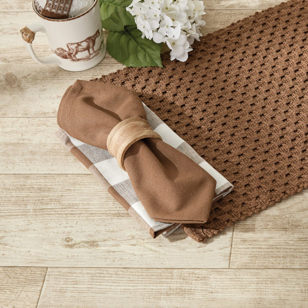 Brown crocheted placemat with a folded napkin on a wooden surface.
