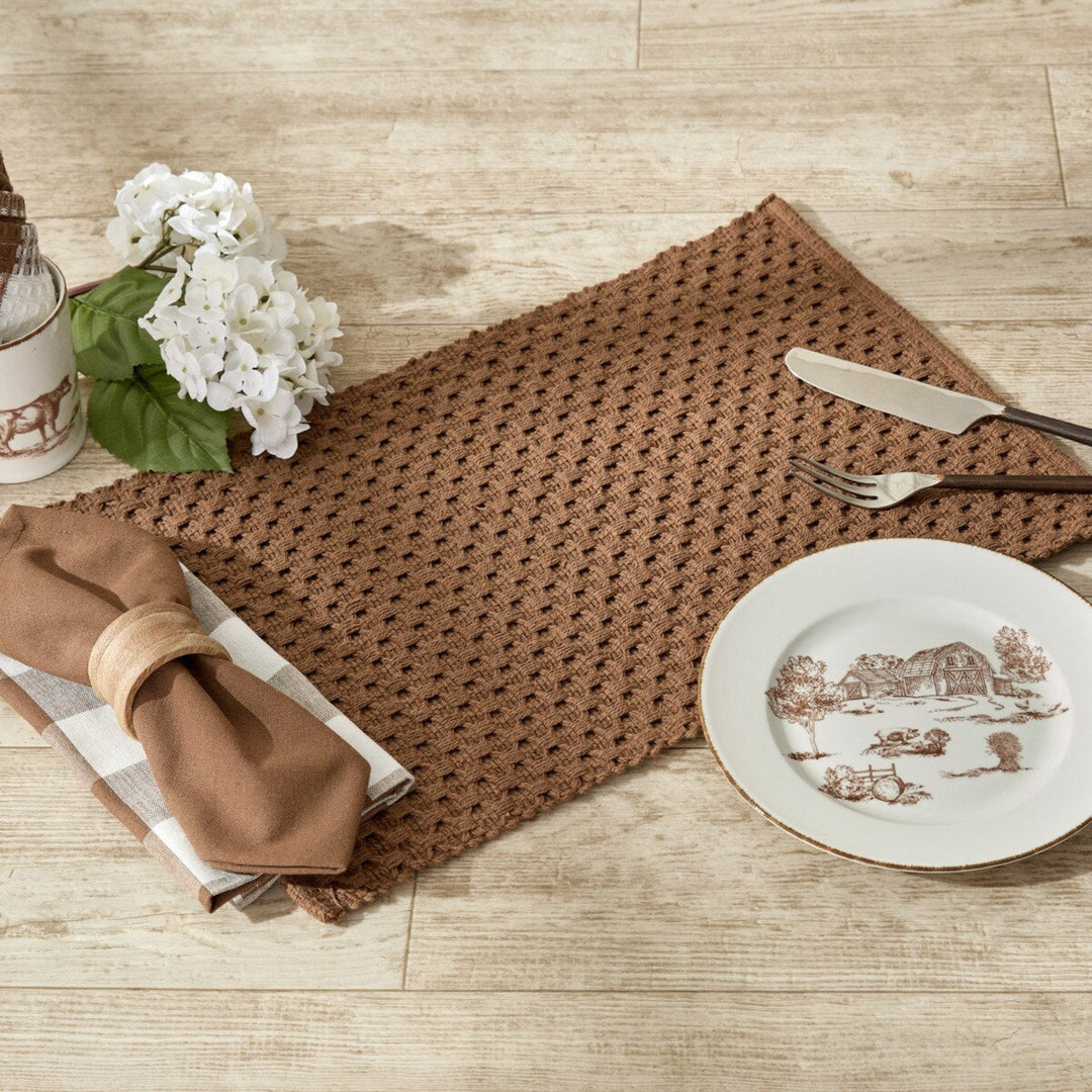 Brown woven placemat on a wooden table with a decorative plate, knife, fork, and napkin.