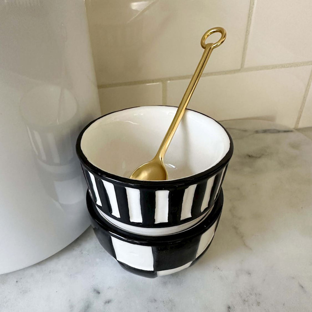 Black and white striped bowl with a gold spoon on a marble surface