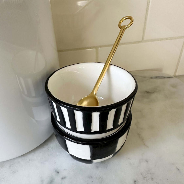 Black and white striped bowl with a gold spoon on a marble surface
