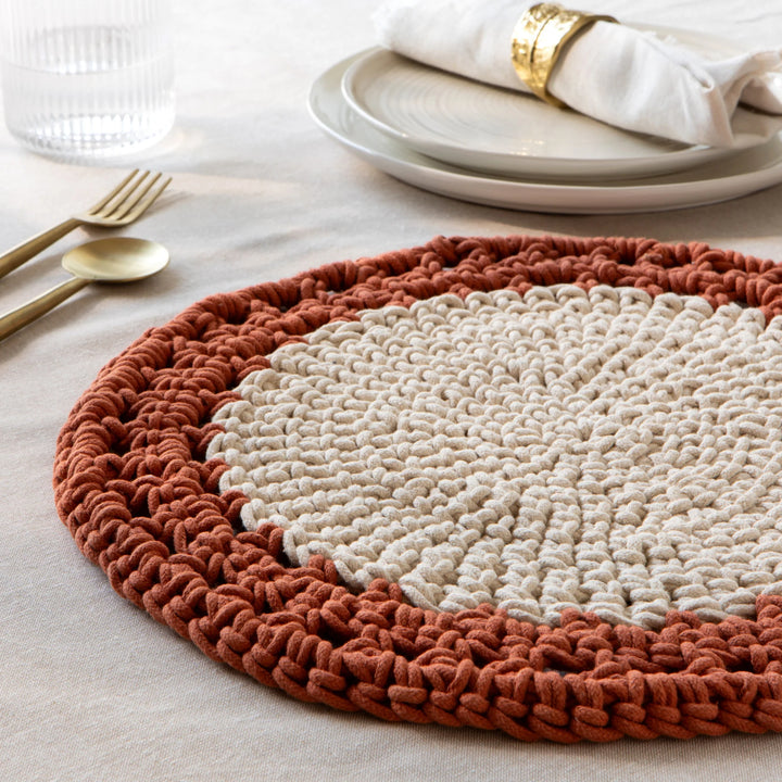 Round woven placemat with two-tone design on a table setting.
