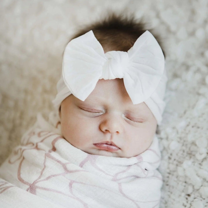Newborn baby wrapped in a patterned blanket with a large white bow on a soft surface
