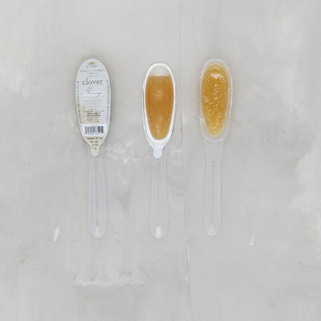Two spoons with honey on a light gray background, one labeled 'clover'.