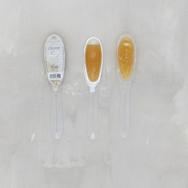 Two spoons with honey on a light gray background, one labeled 'clover'.