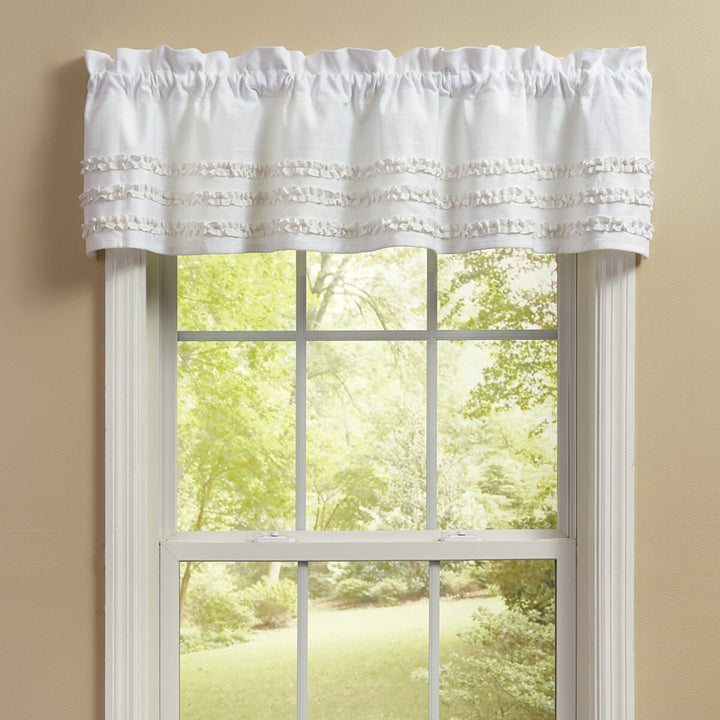 White window valance with ruffled edge on a window with a view of trees.