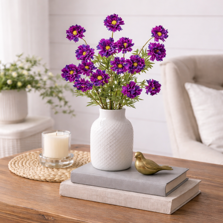 White vase with purple flowers on a stack of books on a wooden table
