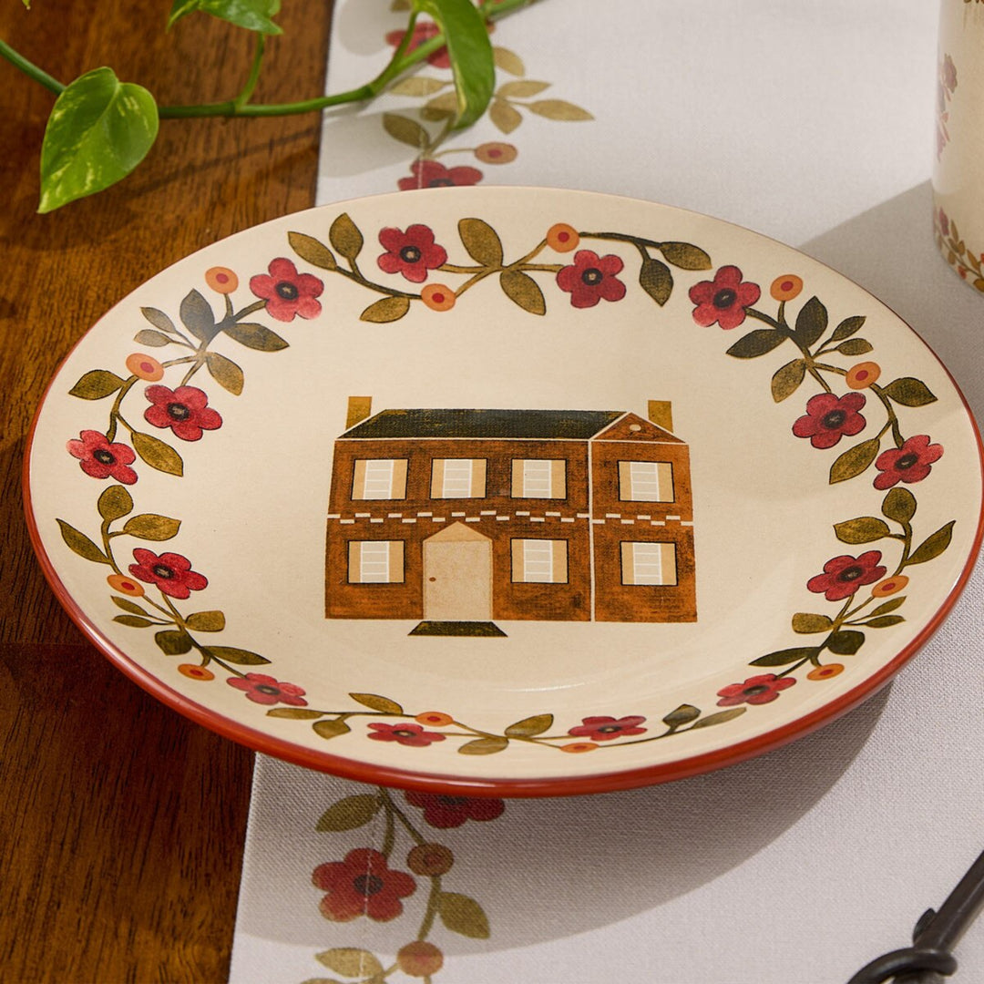 Decorative plate with floral design and house illustration on a table.