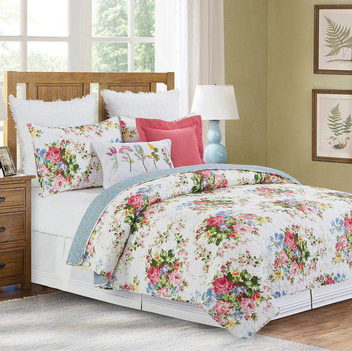 Floral bedding set on a bed in a bedroom with a lamp and framed pictures.