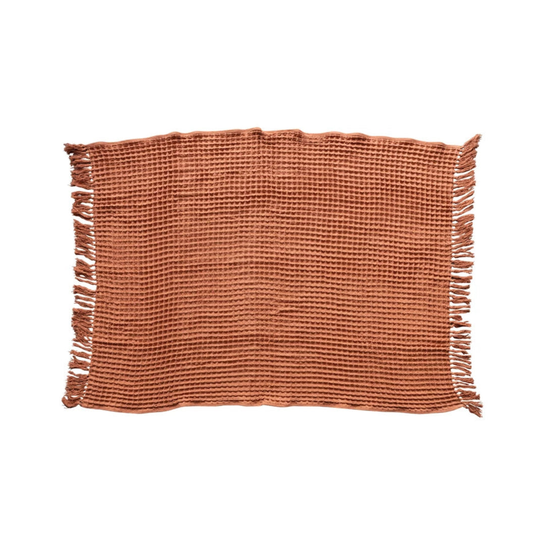 Rust woven placemat with fringes on a white background