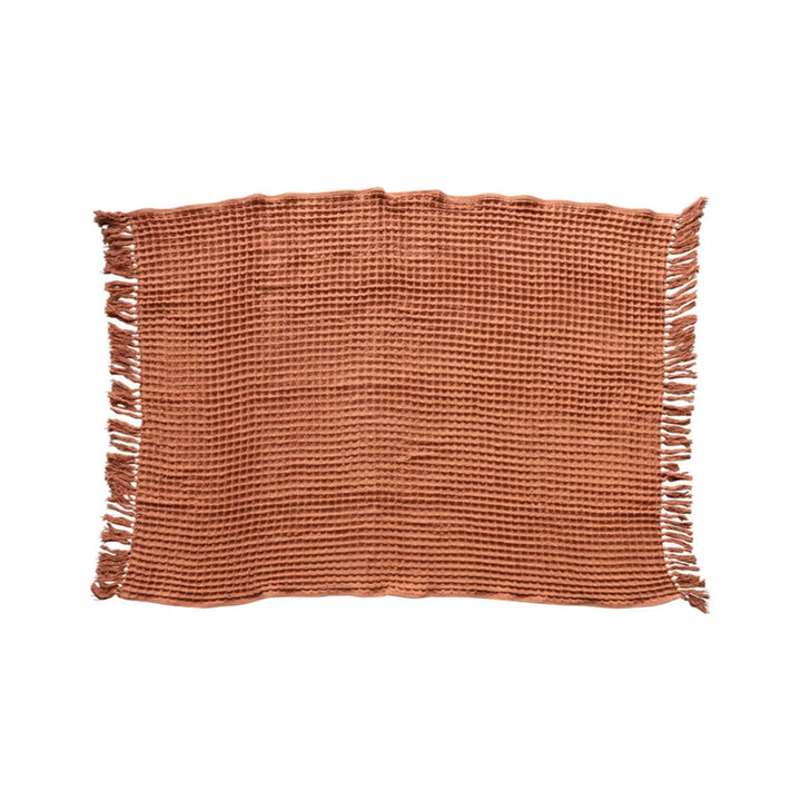 Rust woven placemat with fringes on a white background