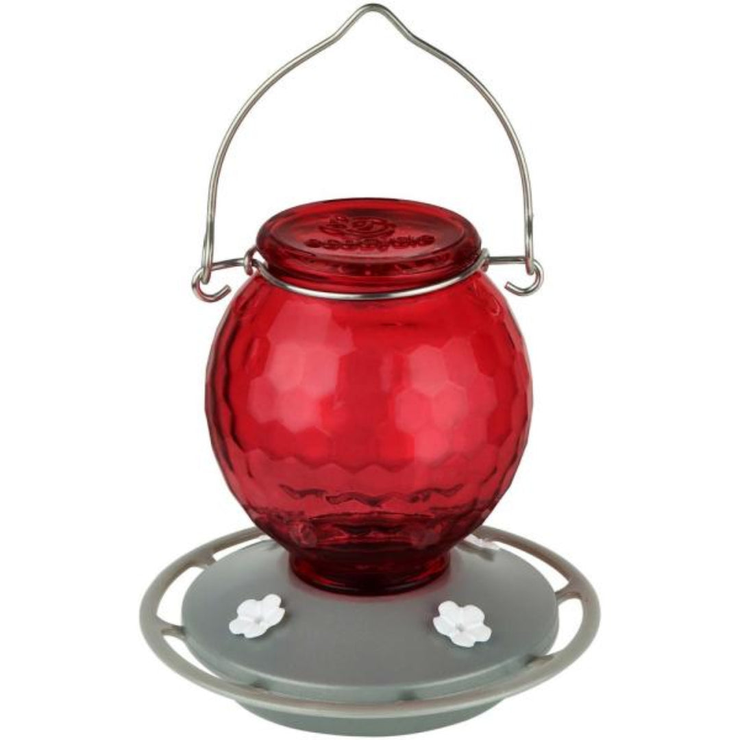 Red glass hummingbird feeder with metal hook on a white background