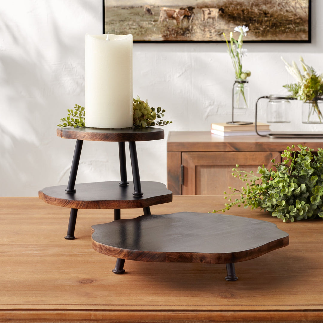 Wooden tiered stand with a candle on a wooden surface, with a painting and decorative items in the background.