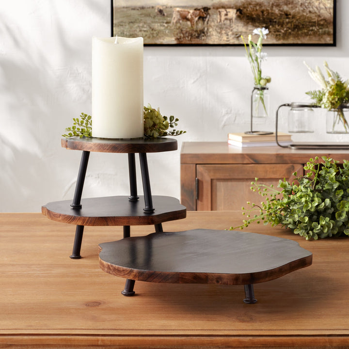 Wooden tiered stand with a candle on a wooden surface, with a painting and decorative items in the background.