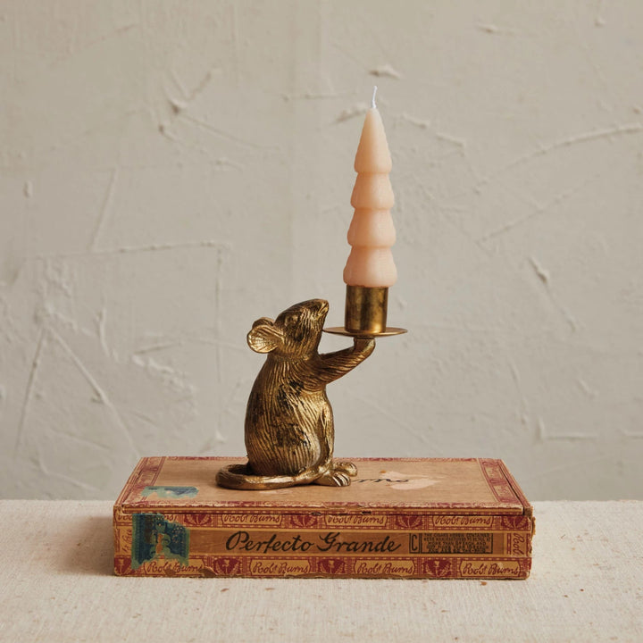 Bronze mouse candle holder with a pink candle on an old book against a textured wall.